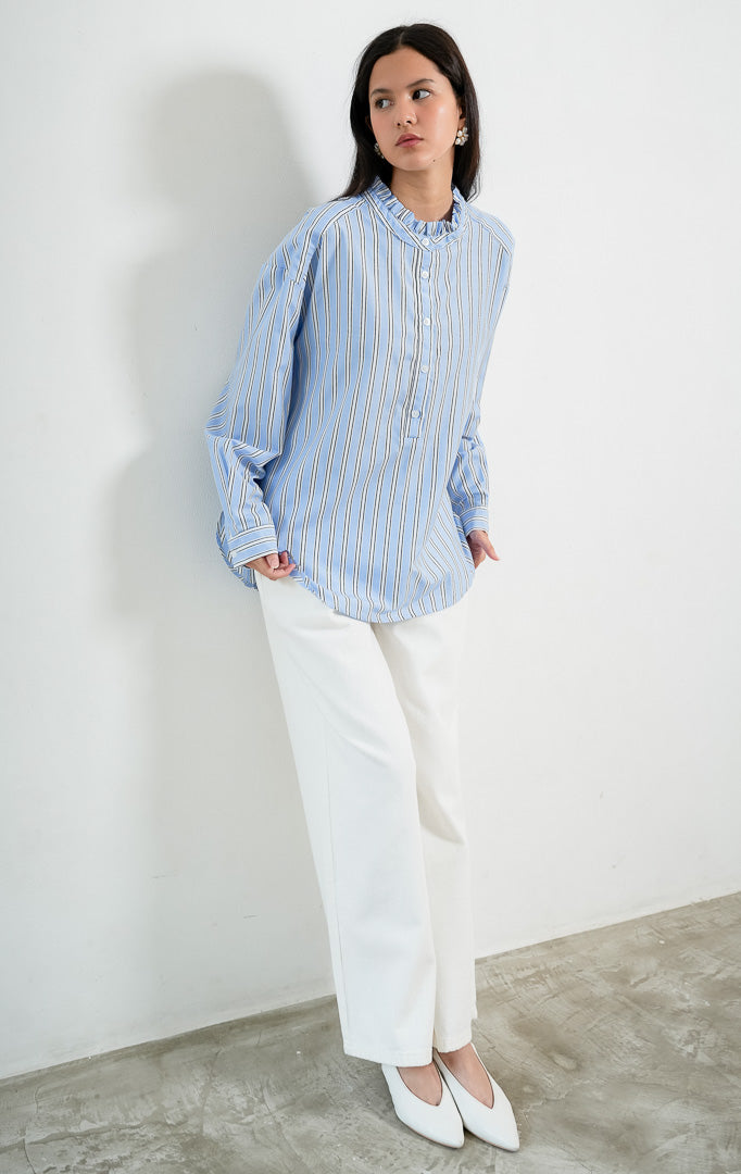 Blus wanita lengan panjang motif garis-garis biru (blue striped) Kellie Top berbahan kain tenun ringan (lightweight woven fabric) dengan kerah berdiri aksen kerut (ruffled stand neckline), bukaan setengah kancing depan (half-placket), dan kelim melengkung (curved hem).