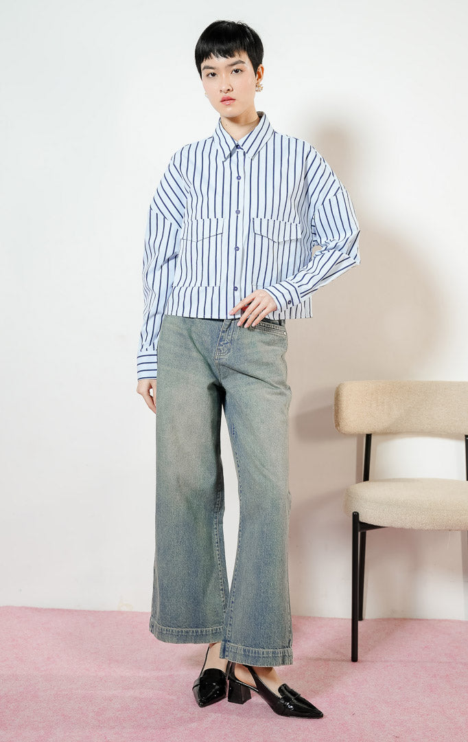 Model wanita mengenakan Georgette Classic Striped Collared Crop Shirt warna light blue, kemeja crop salur wanita lengan panjang berwarna biru muda dengan dua saku depan. 