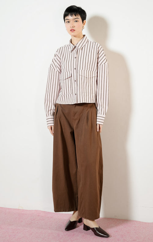 Model wanita mengenakan Georgette Classic Striped Collared Crop Shirt warna light pink, kemeja crop salur wanita lengan panjang berwarna merah muda dengan dua saku depan. 