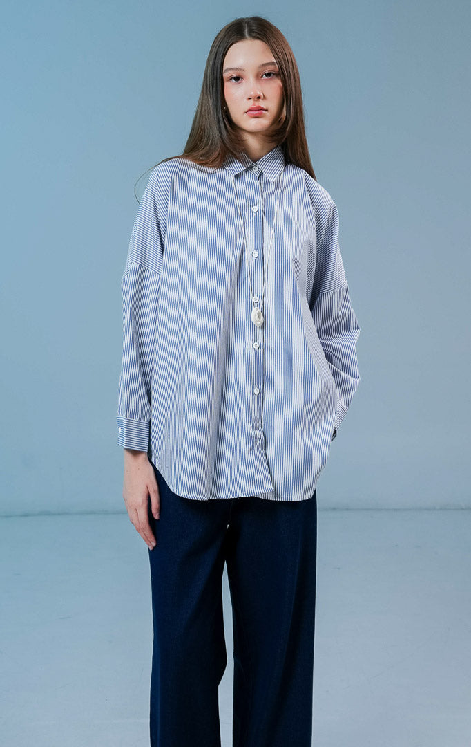 Model wanita mengenakan Dayle Top warna dark blue stripe, kemeja lengan panjang berpotongan longgar dengan motif garis-garis biru dan kancing depan.
