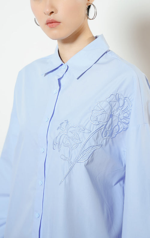 Detail dekat model mengenakan Zinnia Floral Embroidery Detail Shirt warna blue, atasan kemeja katun wanita lengan panjang warna biru muda dengan bordir motif bunga peony minimalis di dada.