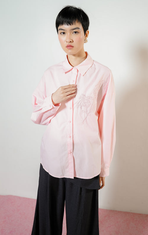 Detail dekat model mengenakan Zinnia Floral Embroidery Detail Shirt warna pink, atasan kemeja katun wanita lengan panjang warna merah muda pastel dengan bordir motif bunga minimalis di dada. 