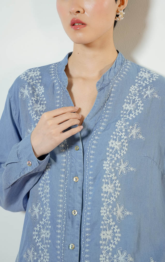 Model wanita mengenakan Brella Embroidery V-Neck Top warna blue denim, kemeja katun wanita lengan panjang berwarna biru muda dengan detail sulaman bordir bunga putih yang anggun. 