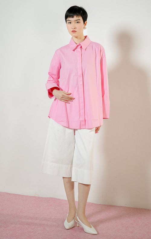 Model wanita mengenakan Monki Essential Basic Shirt warna pink, atasan kemeja katun wanita lengan panjang berpotongan oversized warna merah muda cerah dengan kancing tersembunyi. 