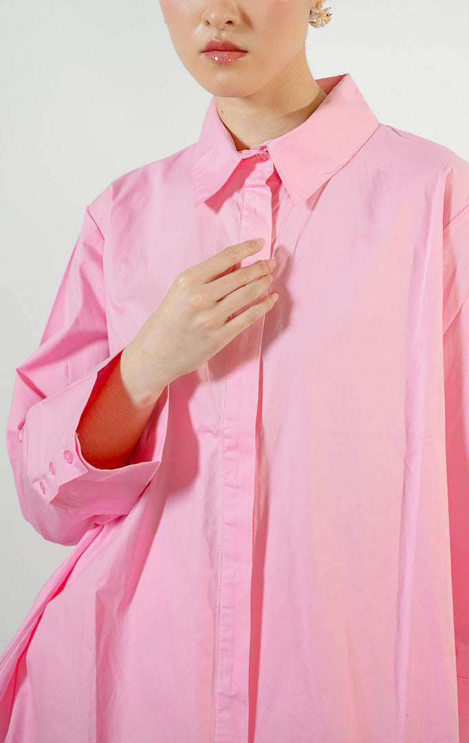 Model wanita mengenakan Monki Essential Basic Shirt warna pink, atasan kemeja katun wanita lengan panjang berpotongan oversized warna merah muda cerah dengan kancing tersembunyi. 