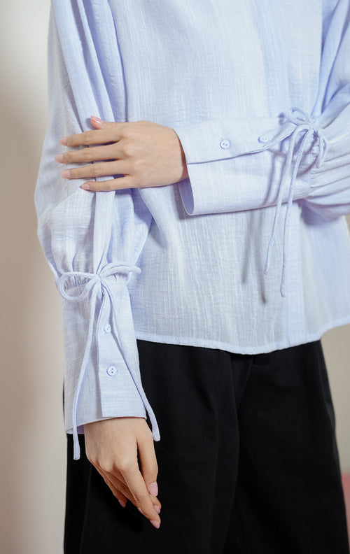 Detail dekat lengan Madden Ribbon-Detail Long-Sleeve Shirt warna blue, kemeja blouse wanita warna biru muda dengan manset panjang berdetail tali pita simpul yang feminin. 