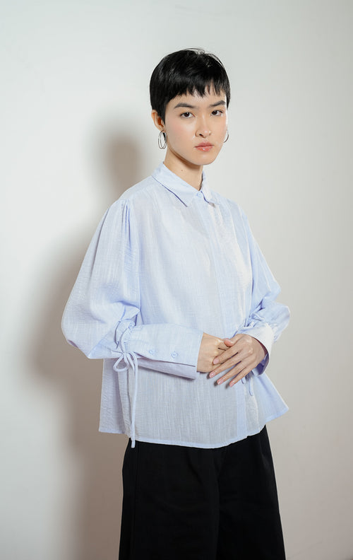 Detail dekat lengan Madden Ribbon-Detail Long-Sleeve Shirt warna blue, kemeja blouse wanita warna biru muda dengan manset panjang berdetail tali pita simpul yang feminin. 