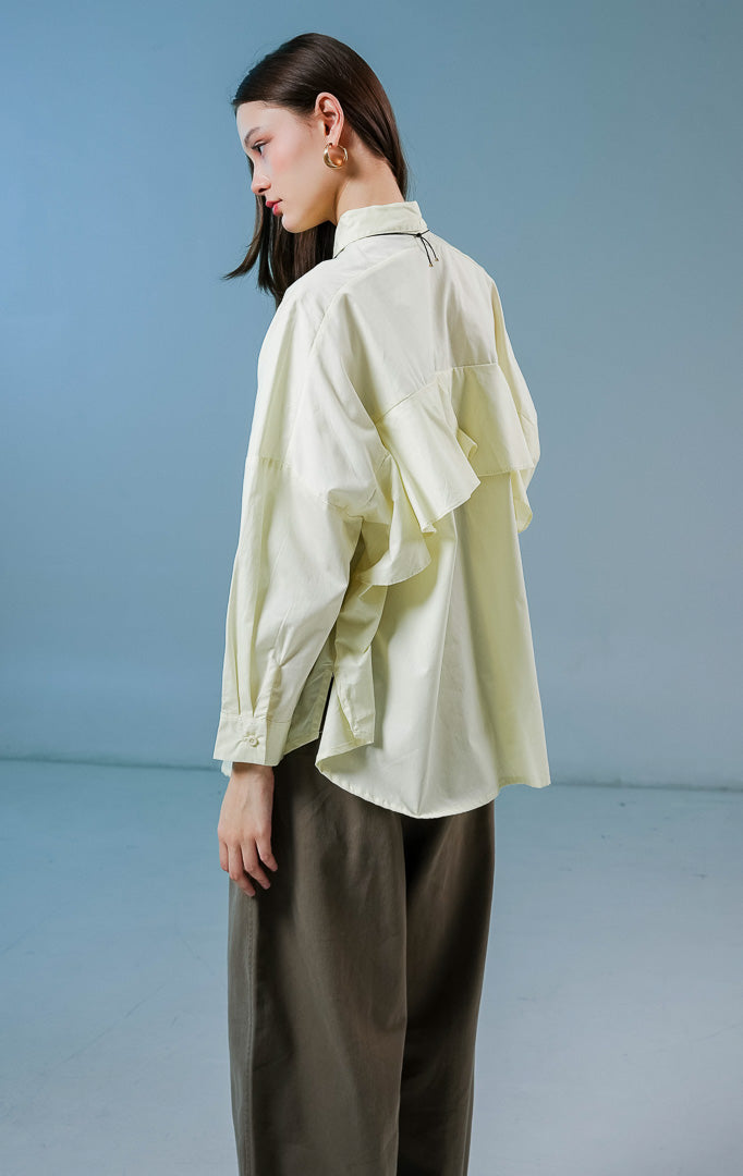 Model wanita mengenakan kemeja lengan panjang Dayle Top warna kuning muda berpotongan longgar (oversize) dengan detail kancing depan. 