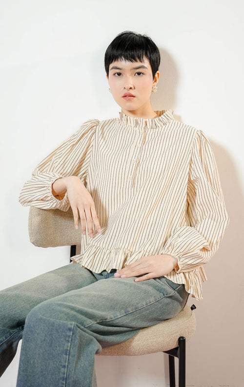 Model wanita mengenakan Alessia Frill-Hem Striped Top warna butter yellow, blouse kemeja salur wanita motif garis kuning dengan detail kerah ruffle dan ujung kelim berkerut yang feminin. 