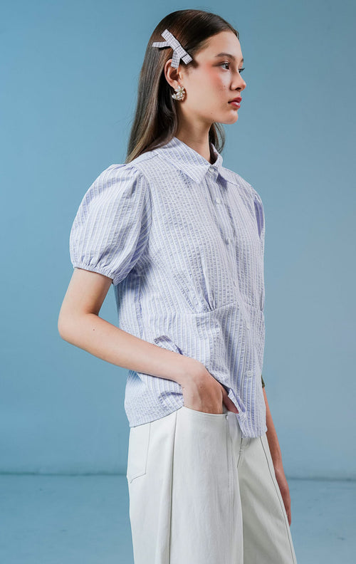 Model wanita mengenakan Theana Collared Puff Sleeve Top warna light purple, blouse kemeja salur wanita motif garis ungu-putih dengan lengan balon pendek dan detail siluet pinggang berstruktur 