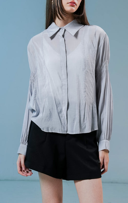 Model wanita mengenakan Milano Gathered Sleeve Collared Sheer Top warna light grey, kemeja lengan panjang transparan wanita dengan detail kerutan lengan yang elegan. 