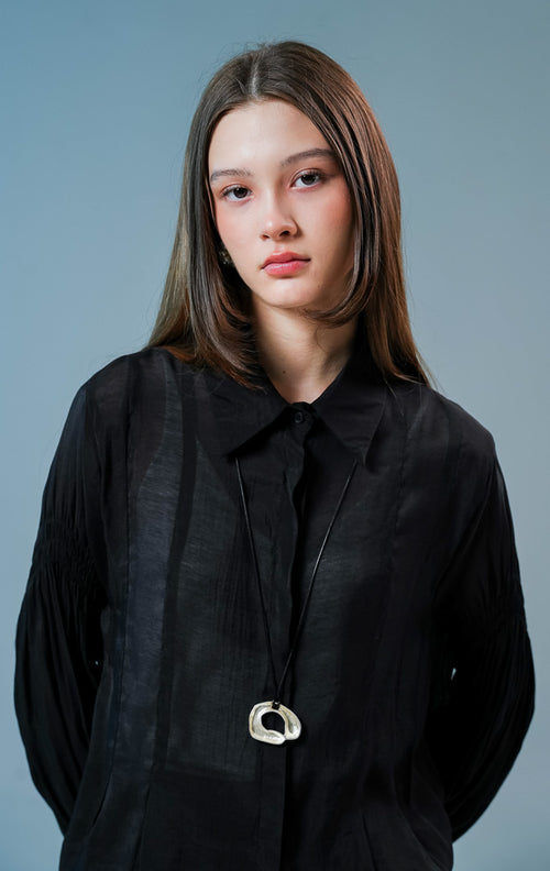 Model wanita mengenakan Milano Gathered Sleeve Collared Sheer Top warna hitam, kemeja lengan panjang transparan wanita dengan detail kerutan lengan yang elegan. 