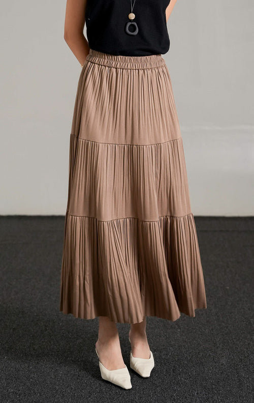 Kenny Skirt Khaki, rok panjang lipit bertingkat warna cokelat khaki dengan detail pinggang karet, dipadukan dengan tank top hitam dan kalung liontin.