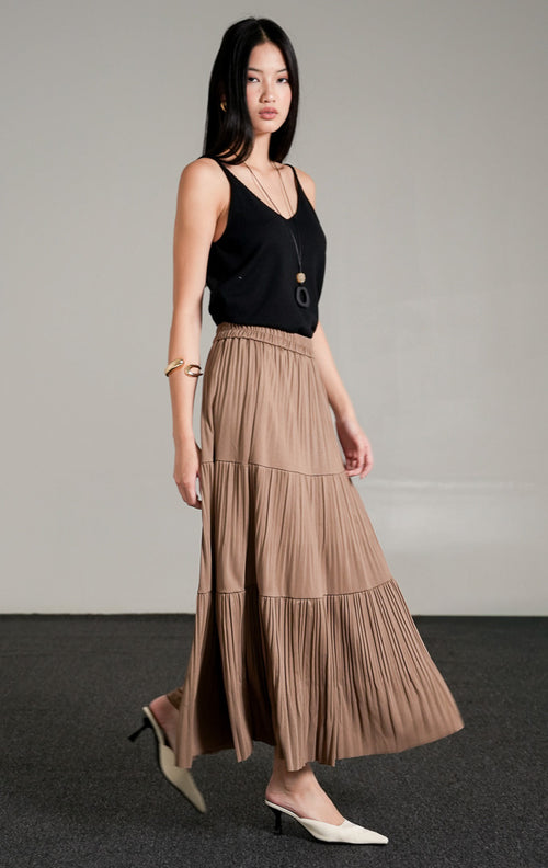 Kenny Skirt Khaki, rok panjang lipit bertingkat warna cokelat khaki dengan detail pinggang karet, dipadukan dengan tank top hitam dan kalung liontin.