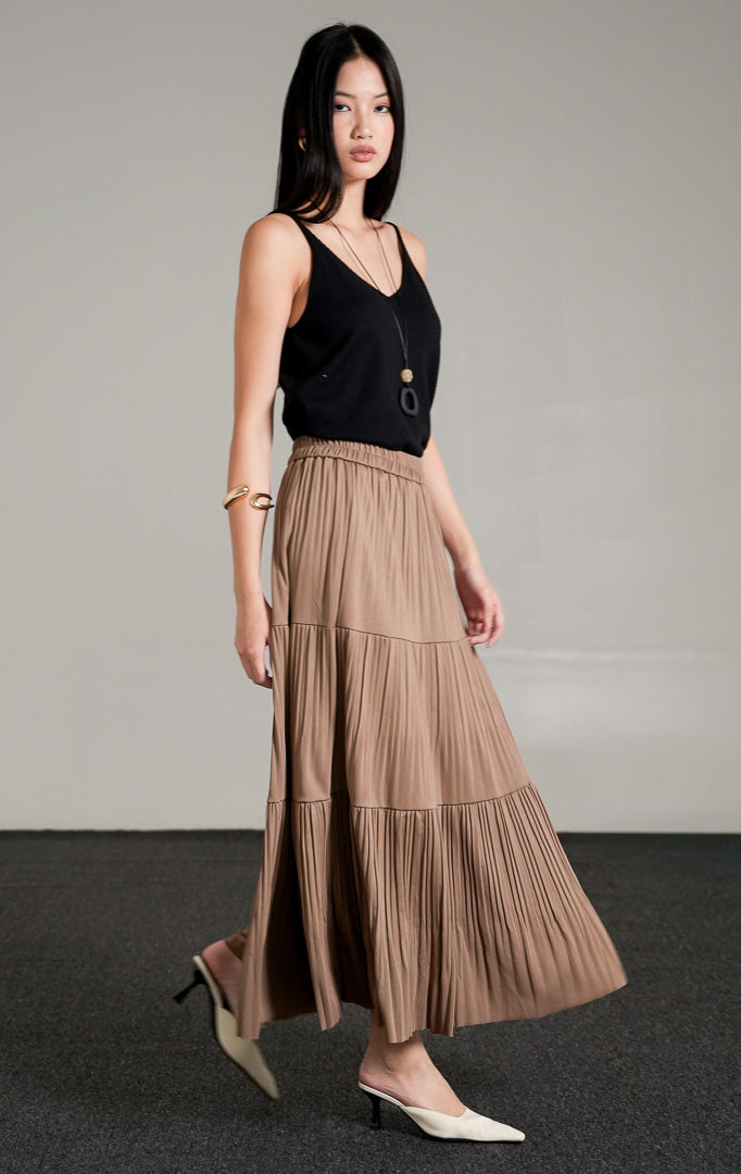 Kenny Skirt Khaki, rok panjang lipit bertingkat warna cokelat khaki dengan detail pinggang karet, dipadukan dengan tank top hitam dan kalung liontin.