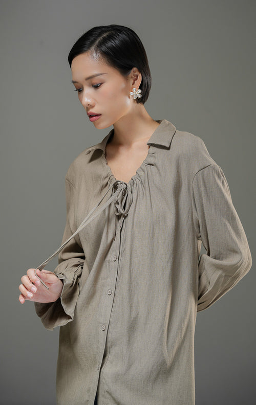Blouse wanita Kensley Top warna brown cokelat lengan panjang dengan detail tali pita leher (tie neck), kerah kemeja, dan kancing depan. 