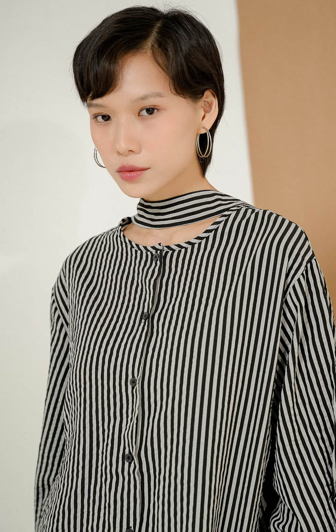 Close up model mengenakan KianoStripe Shirt Black, kemeja salur wanita lengan panjang motif garis hitam-abu dengan detail cut-out dan strap unik di bagian leher. 