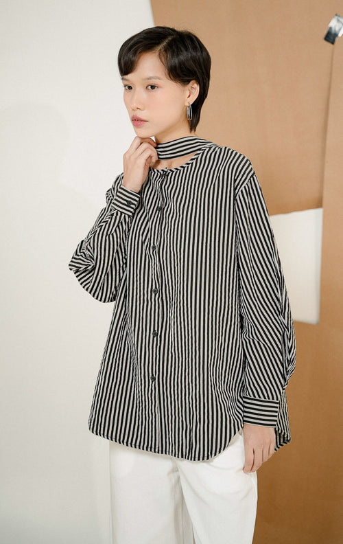 Close up model mengenakan KianoStripe Shirt Black, kemeja salur wanita lengan panjang motif garis hitam-abu dengan detail cut-out dan strap unik di bagian leher. 