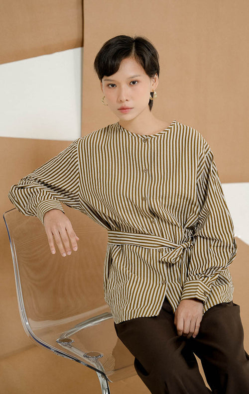 Model berdiri mengenakan Kiano Waist Tie Stripe Shirt Brown, kemeja salur wanita lengan panjang motif garis cokelat-putih dengan detail tali ikat di pinggang dipadukan celana kulot panjang.