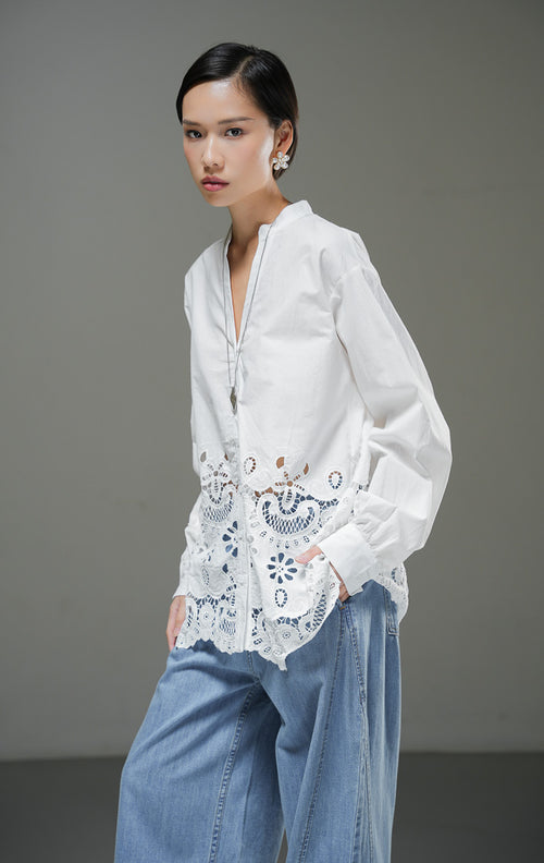 Kemeja wanita Kiraya Top warna putih lengan panjang dengan kerah sanghai V-neck dan detail bordir eyelet renda mewah di bagian bawah hem. 