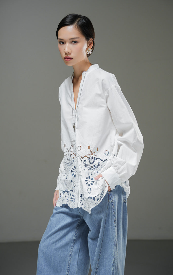 Kemeja wanita Kiraya Top warna putih lengan panjang dengan kerah sanghai V-neck dan detail bordir eyelet renda mewah di bagian bawah hem. 