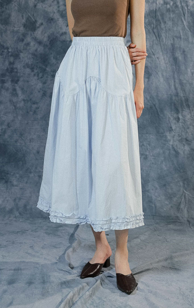 Rok panjang (maxi skirt) wanita Lacey warna biru berbahan katun dengan detail tingkat (tiered), jahitan bergelombang di tengah, aksen ruffle bawah, dan pinggang karet.