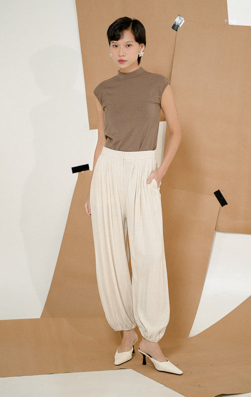 Model berdiri mengenakan Lachlan Relaxed Linen Blend Pants Ivory, produk celana panjang linen wanita warna krem ivory dengan kerutan karet di pergelangan kaki 