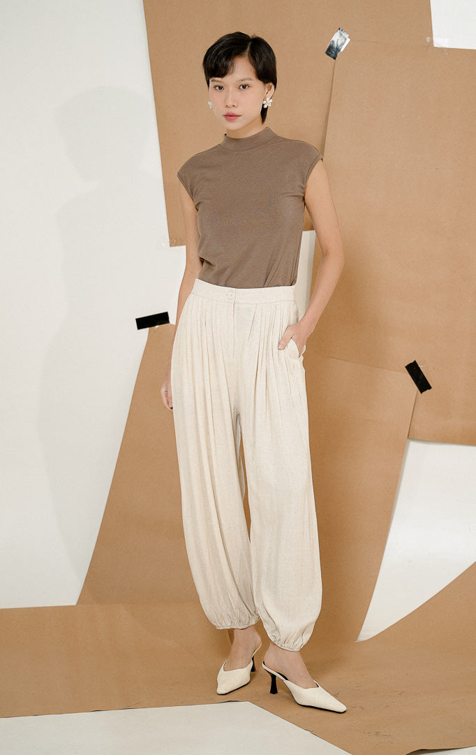 Model berdiri mengenakan Lachlan Relaxed Linen Blend Pants Ivory, produk celana panjang linen wanita warna krem ivory dengan kerutan karet di pergelangan kaki 