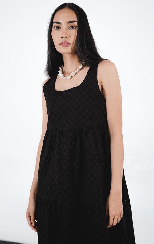 Model wanita mengenakan Layila Dress warna black, gaun mini tanpa lengan dengan detail bordir eyelet bermotif floral di seluruh bagian kain