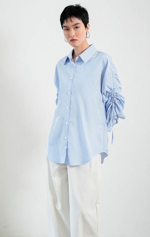 Kemeja wanita lengan panjang warna biru (blue) motif garis halus Liliana Top dengan kerah klasik (classic collar), bukaan kancing depan, dan detail tali serut pada bagian lengan (adjustable ruched sleeves with drawstring ties). 