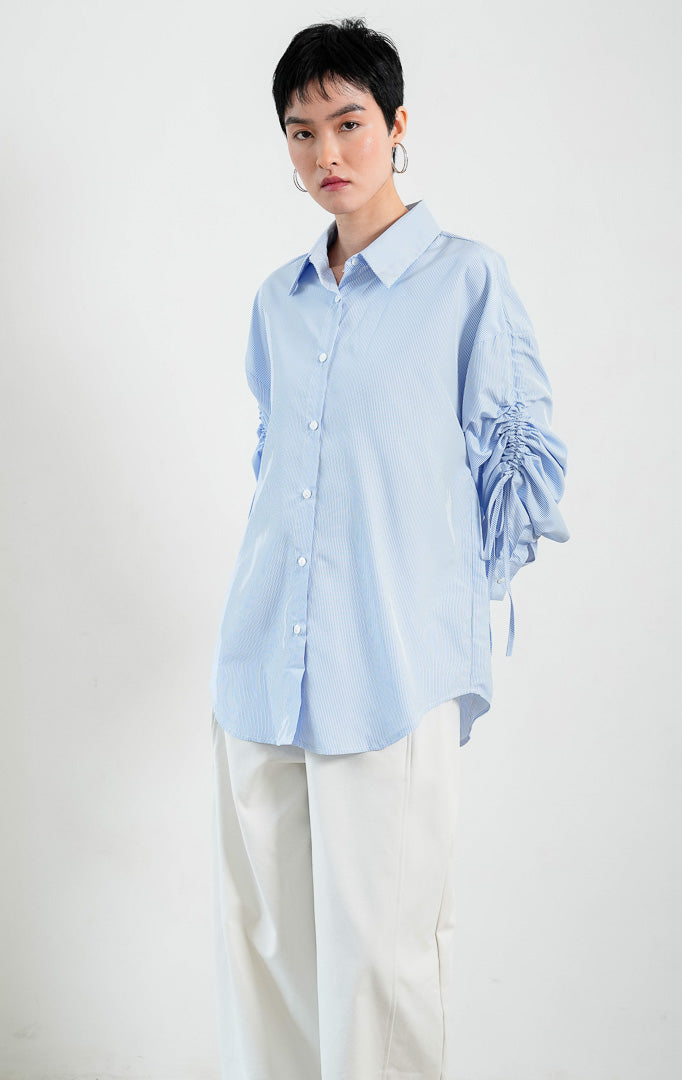 Kemeja wanita lengan panjang warna biru (blue) motif garis halus Liliana Top dengan kerah klasik (classic collar), bukaan kancing depan, dan detail tali serut pada bagian lengan (adjustable ruched sleeves with drawstring ties). 
