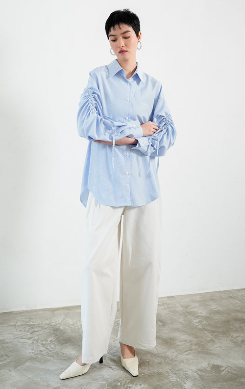 Kemeja wanita lengan panjang warna biru (blue) motif garis halus Liliana Top dengan kerah klasik (classic collar), bukaan kancing depan, dan detail tali serut pada bagian lengan (adjustable ruched sleeves with drawstring ties). 