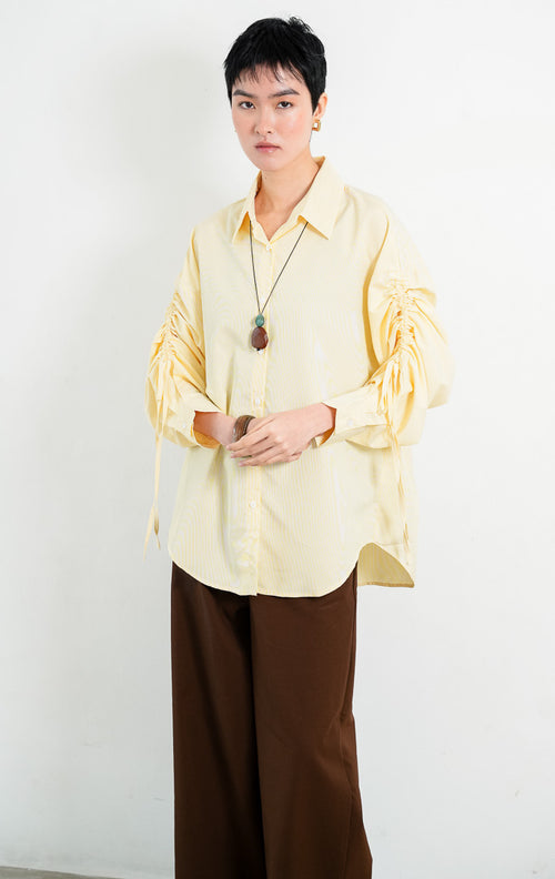 Kemeja wanita lengan panjang warna kuning (yellow) motif garis halus Liliana Top dengan kerah klasik (classic collar), bukaan kancing depan, dan detail tali serut pada bagian lengan (adjustable ruched sleeves with drawstring ties). 