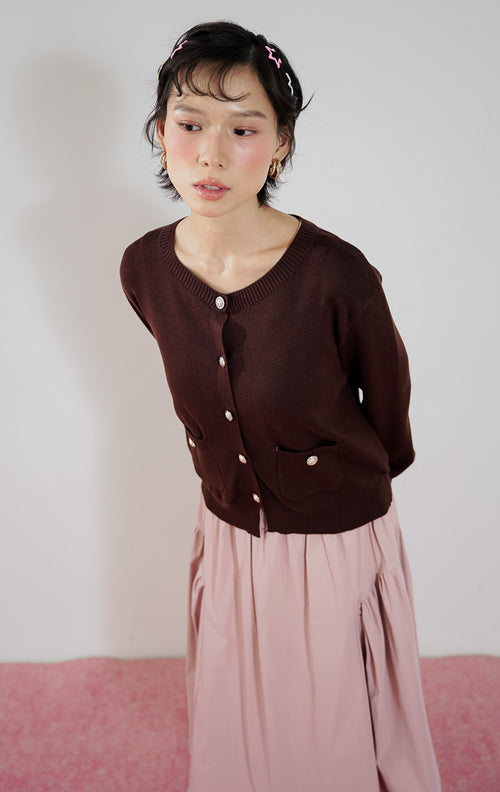 Kardigan rajut wanita Lily Cardigan warna cokelat tua (brown) dari This Is April dengan detail kancing emas dan kantong depan, dipadukan dengan rok midi pink.