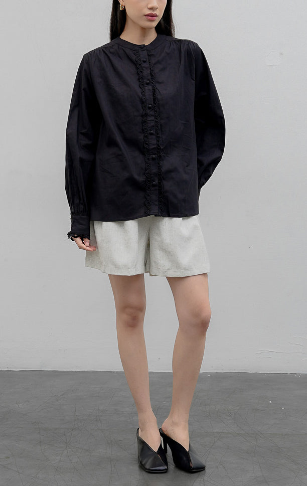 Kemeja wanita lengan panjang warna hitam (black) Lois Top berbahan katun terstruktur (structured cotton) dengan kerah sanghai (stand collar), aksen bordir berlubang (voile eyelet detailing), dan bukaan kancing depan.