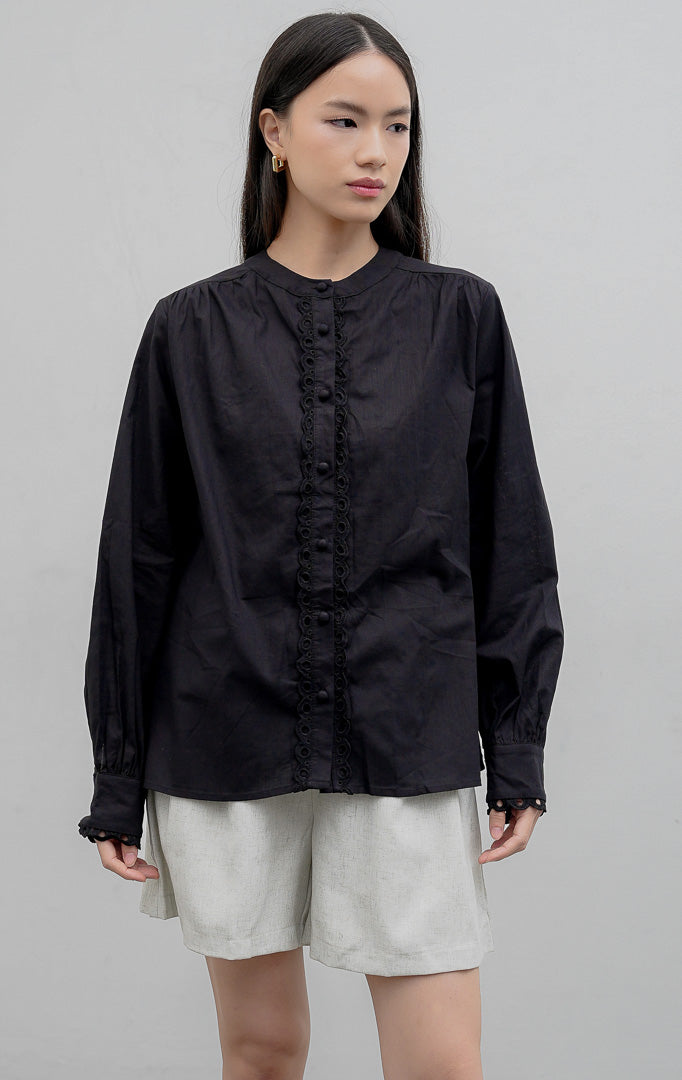 Kemeja wanita lengan panjang warna hitam (black) Lois Top berbahan katun terstruktur (structured cotton) dengan kerah sanghai (stand collar), aksen bordir berlubang (voile eyelet detailing), dan bukaan kancing depan.