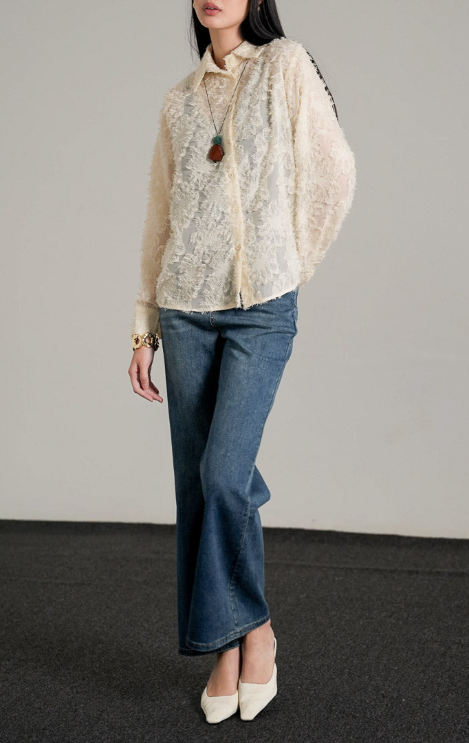 Loui Top Ivory, kemeja lengan panjang warna putih tulang semi-transparan dengan tekstur bulu halus, dipadukan dengan celana jeans biru.