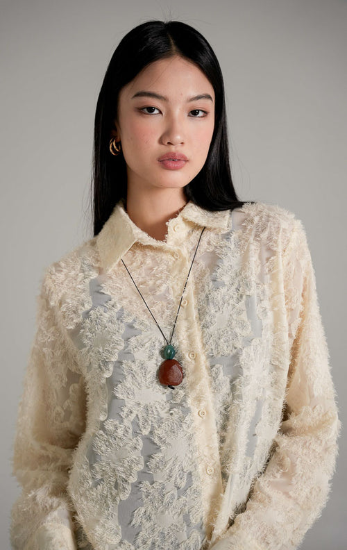 Loui Top Ivory, kemeja lengan panjang warna putih tulang semi-transparan dengan tekstur bulu halus, dipadukan dengan celana jeans biru.