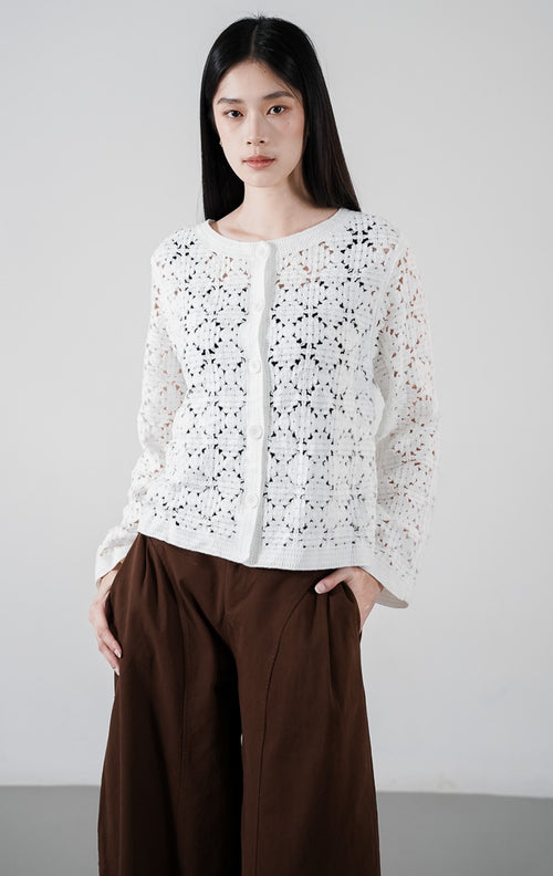 Model mengenakan Lucia Cardigan warna white, kardigan lengan panjang bahan rajut kait (crochet knit) motif floral transparan dengan kancing depan putih.