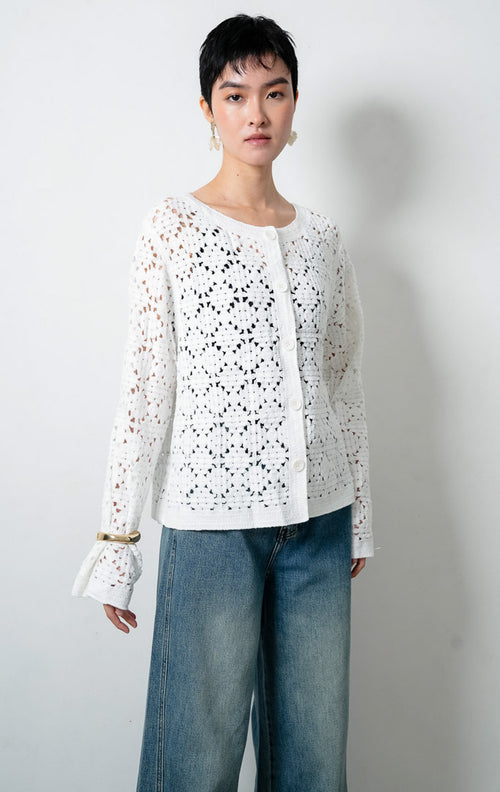 Kardigan rajut wanita lengan panjang warna putih (white) Lucia Cardigan berbahan rajut renda transparan (crochet open-knit) dengan kerah bulat (round neckline) dan bukaan kancing depan warna senada.