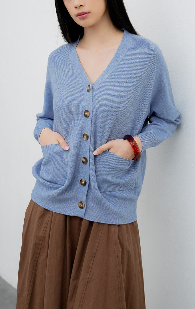 Kardigan rajut wanita model longgar (oversized) warna biru muda (light blue) Lumora Cardigan dengan kerah V (V-neck), dua saku depan fungsional, dan bukaan kancing.
