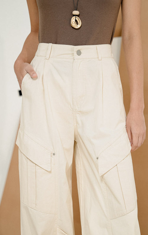 Model berpose dari samping mengenakan Lunaria Utility Bush Pants Ivory, produk celana panjang cargo wanita warna putih gading dengan detail saku utilitas samping 