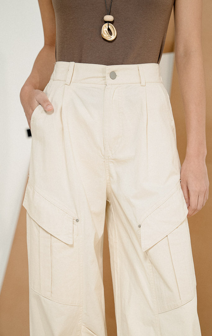 Model berpose dari samping mengenakan Lunaria Utility Bush Pants Ivory, produk celana panjang cargo wanita warna putih gading dengan detail saku utilitas samping 