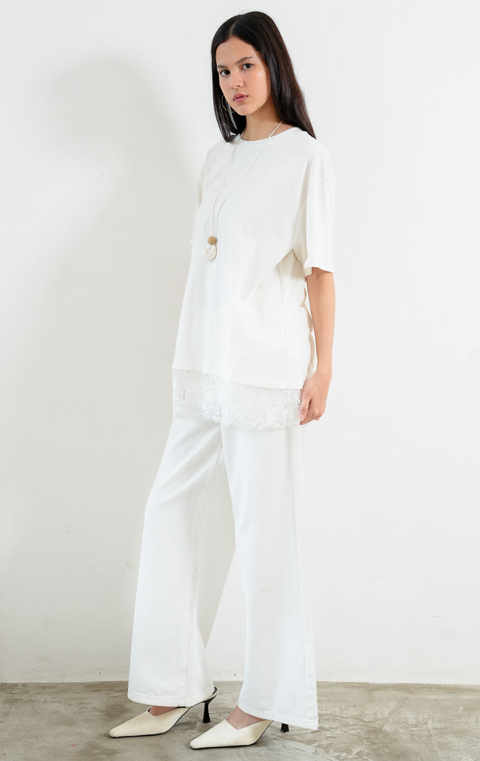 Kaos wanita lengan pendek warna putih (white T-shirt) Lyora Top dengan siluet santai (relaxed silhouette), kerah bulat, dan detail aksen hiasan renda halus di bagian kelim bawah (delicate lace hem detail). 