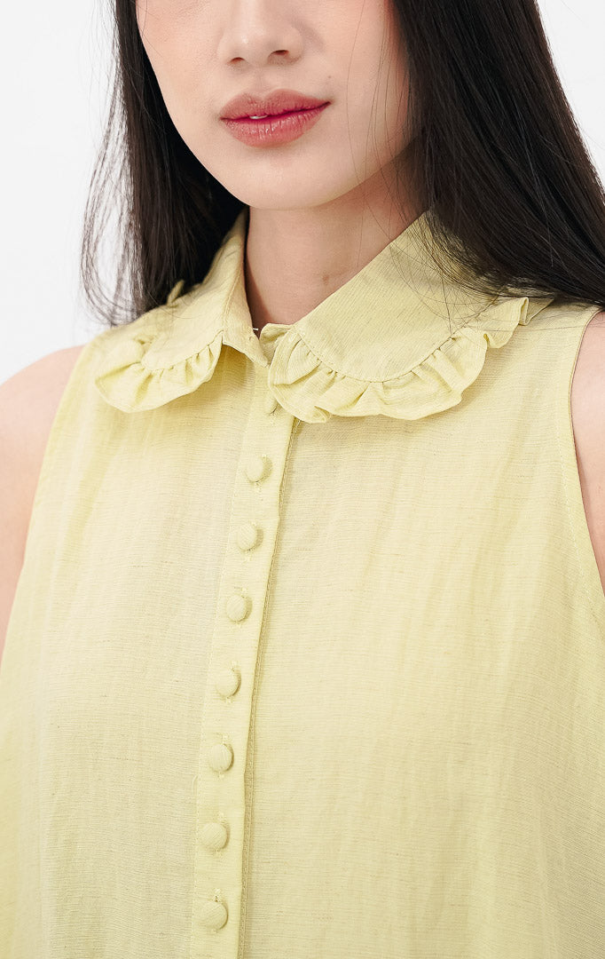 Model mengenakan Malou Top warna yellow, atasan katun tanpa lengan dengan kerah ruffle, kancing bungkus depan, serta detail bordir eyelet dan ruffle pada ujung bawah.