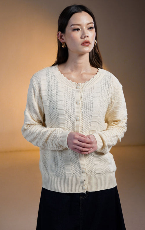 Model wanita mengenakan Margaret Knit Cardigan warna Ivory (putih gading), outer rajut lengan panjang bertekstur dengan kancing bungkus senada dan kerah bulat bergelombang (scalloped neckline).