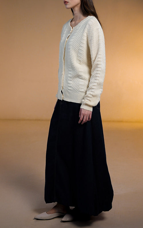 Model wanita mengenakan Margaret Knit Cardigan warna Ivory (putih gading), outer rajut lengan panjang bertekstur dengan kancing bungkus senada dan kerah bulat bergelombang (scalloped neckline).