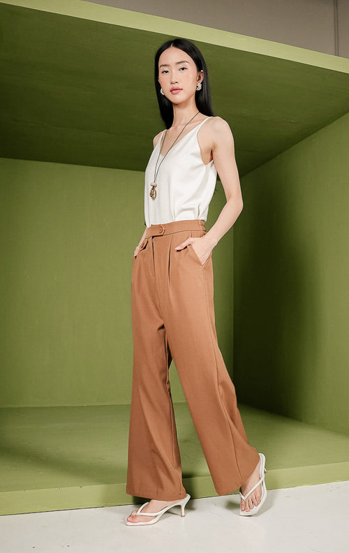 Celana panjang wanita Margo Pants berpotongan lurus (straight cut) warna cokelat camel, dilengkapi detail aksen lipatan kancing unik pada ban pinggang depan sebelah kiri, saku samping, serta karet elastis di pinggang bagian belakang.