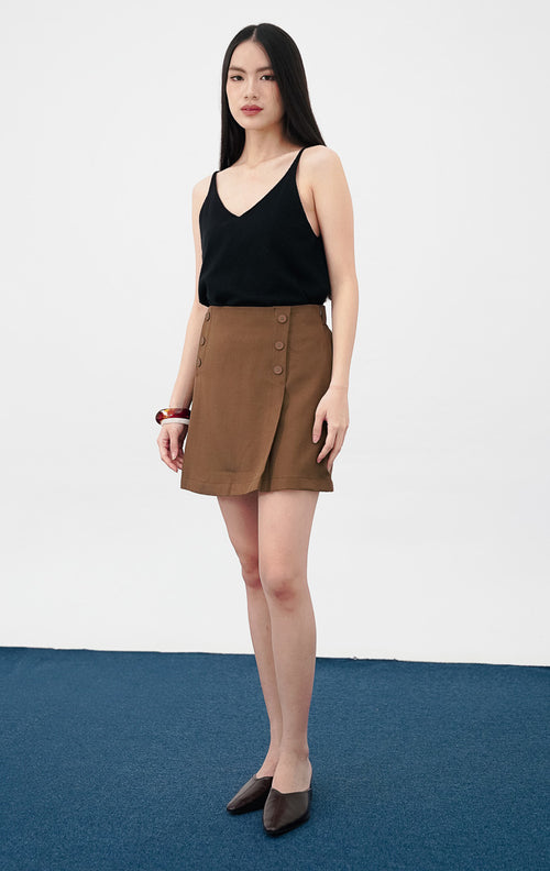 Model mengenakan Matteo Skort warna dark brown, rok celana pendek dengan detail deretan kancing dekoratif di sisi depan dan potongan pinggang tinggi (high-waist).