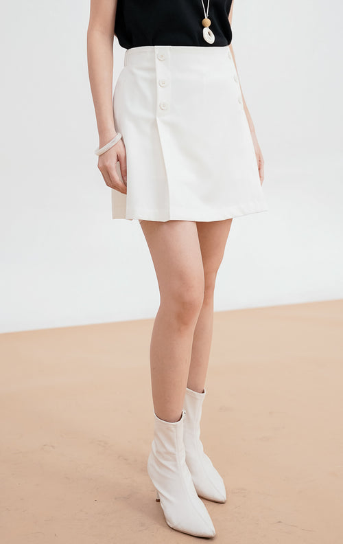 Model mengenakan Matteo Skort warna white, rok celana dengan detail dua baris kancing dekoratif di sisi depan, dipadukan dengan sepatu bot putih.